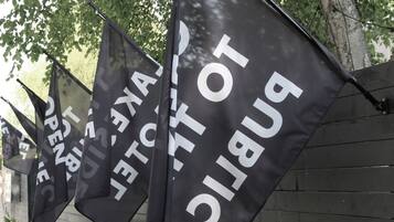 Multiple black flags with white text hanging from a structure.