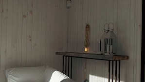 A room with a wooden wall, a white sofa, a small table with a lamp, and a hanging light fixture.