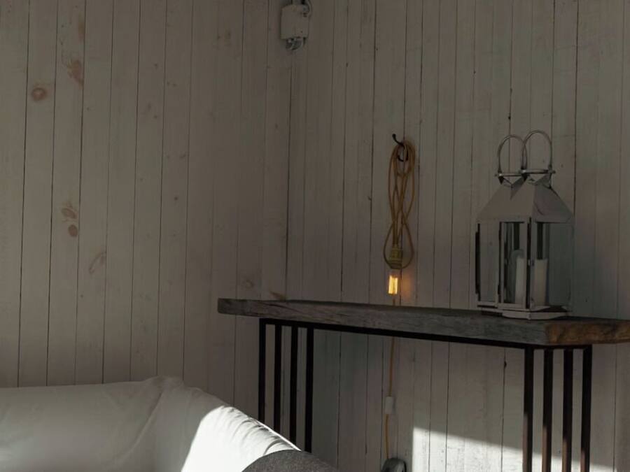 Una habitación con pared de madera, un sofá blanco, una mesita con lámpara y una lámpara colgante.