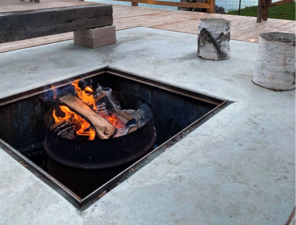 A fire pit with burning logs on a concrete patio.