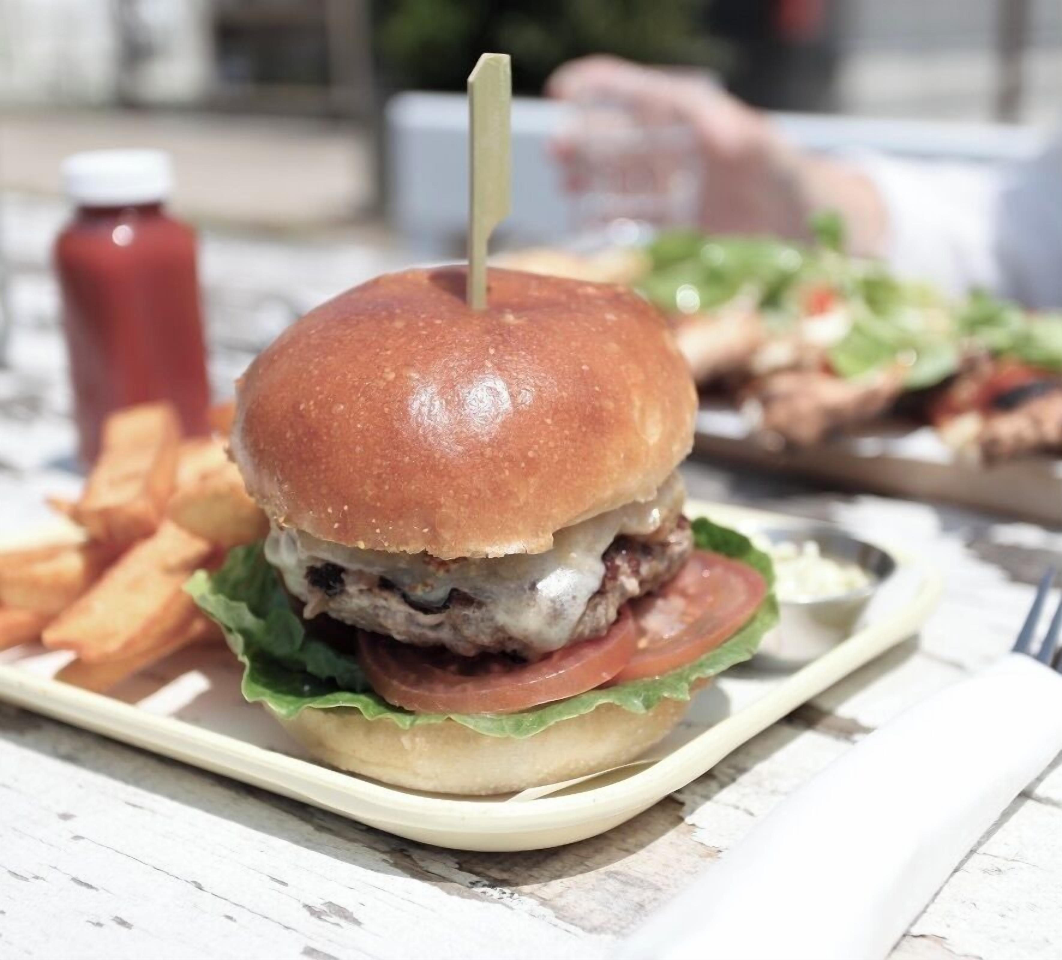 Hamburguesa con un palillo sobre un plato, acompañada de papas fritas y una botella de kétchup.