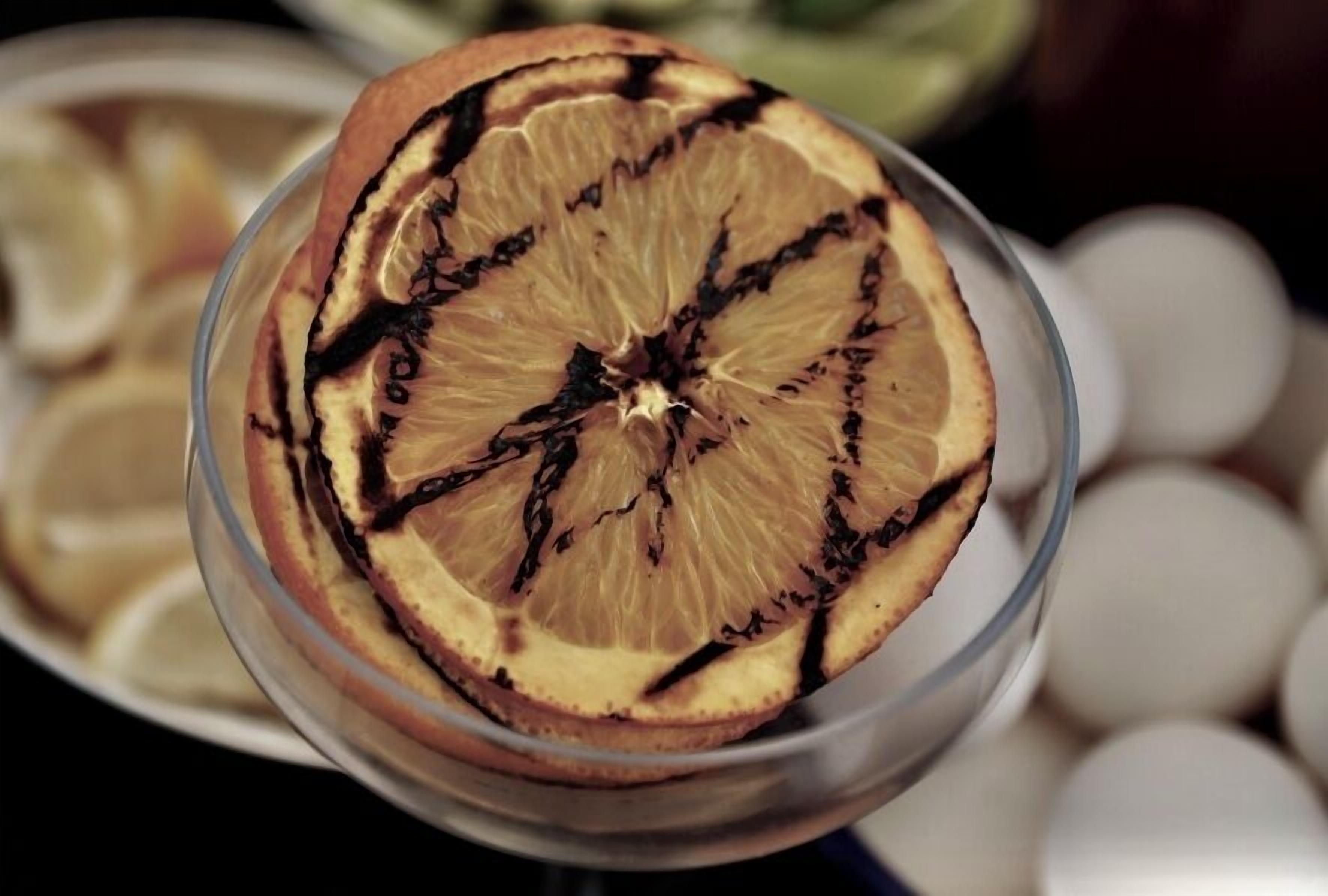 A glass containing a dried slice of citrus fruit with darkened edges.