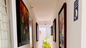 A hallway with tiled flooring, framed artwork on the walls, and potted plants at the end.