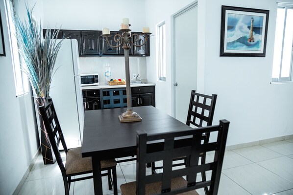 A dining area with a dark wooden table and chairs, a tall floor lamp, and a kitchen in the background. - El Rincon De Los Angeles (Colima)