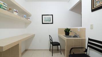 A small kitchen with a sink, a chair, and a shelf with food items.