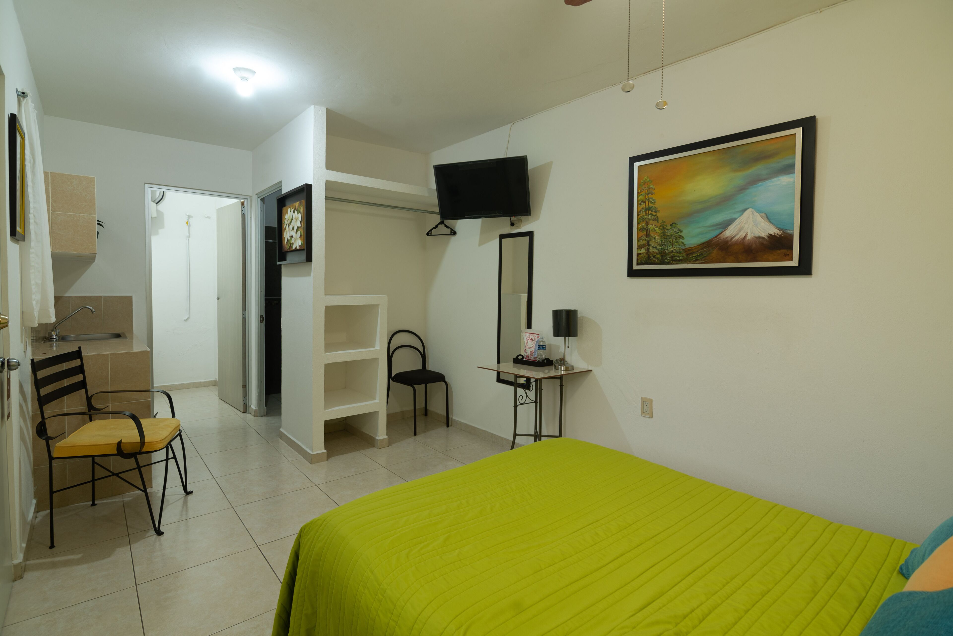 Habitación de hotel con cama, una silla, un escritorio, televisor y un cuadro en la pared.