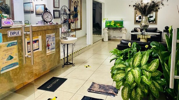 A hotel lobby with a reception desk, a television, a ceiling fan, and a large potted plant.