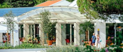 Un edificio moderno con un vestíbulo cubierto, plantas en macetas y un cartel que indica la zona de recepción.