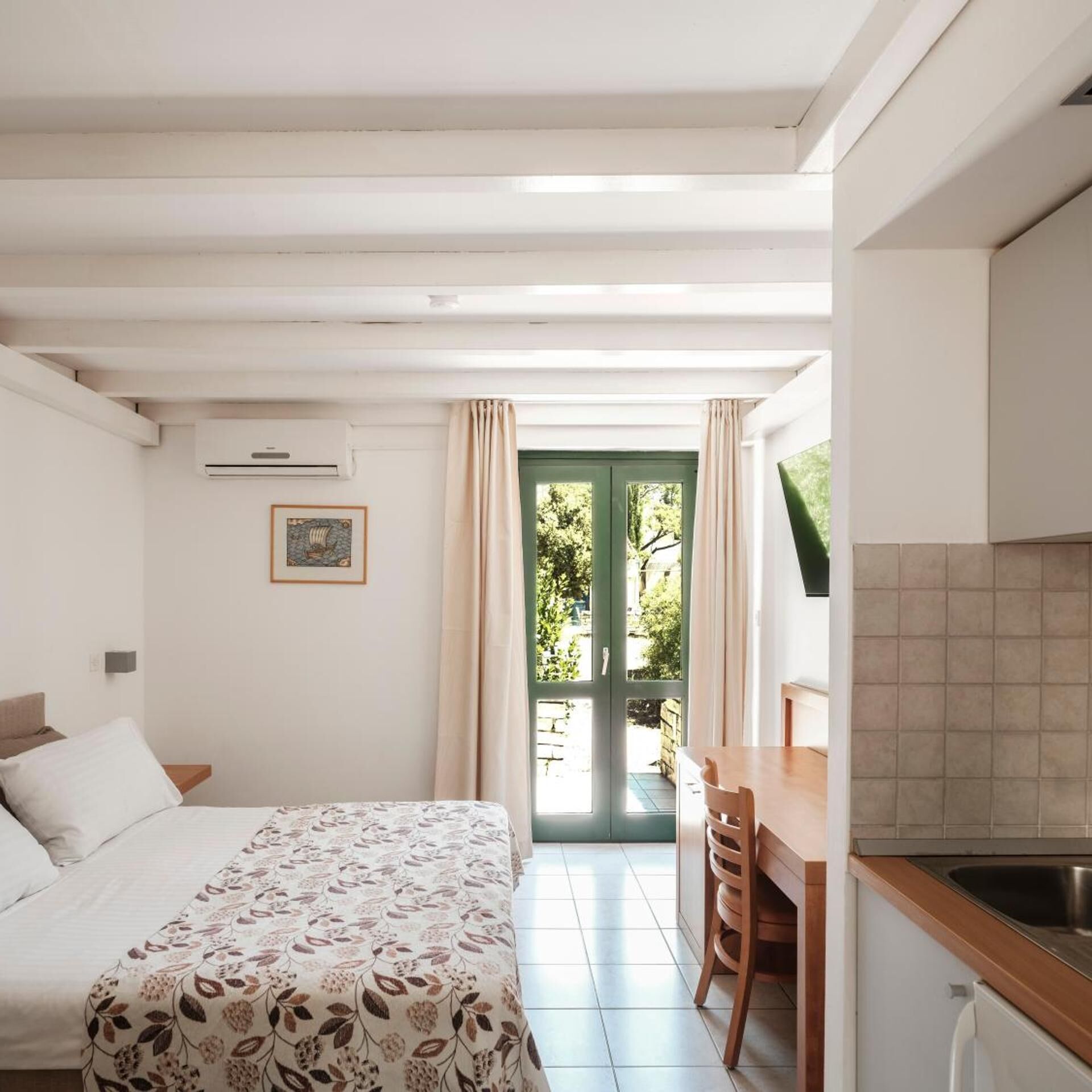 A bedroom with a bed, a desk, and a view of the outdoors.
