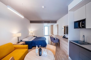 A hotel room with a bed, a desk, a chair, a table with drinks, a sofa, a lamp, a microwave, and a sink. - Zaton Holiday Resort (Nin)