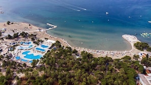Vista aérea de un complejo turístico costero con una gran piscina, zonas de playa y un puerto deportivo.