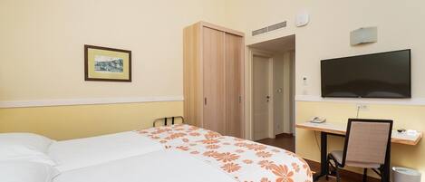 A hotel room with a bed, a desk with a chair, a television, and a framed picture on the wall.