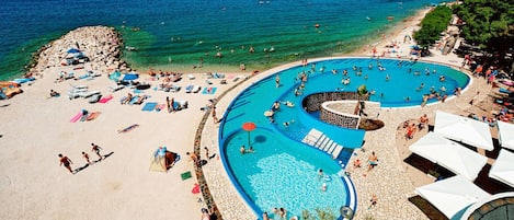 Una spiaggia con una grande piscina, lettini e ombrelloni.