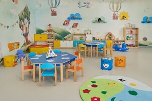Uma sala de jogos infantil com mobiliário colorido, uma mesa de brincar e diversos brinquedos.
