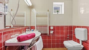 Un baño con un lavamanos blanco, una toalla rosa, un inodoro blanco y un perchero.