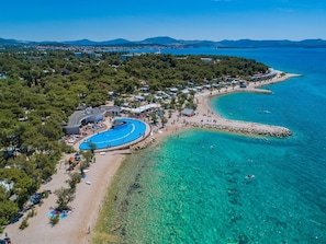 Vista aérea de un complejo turístico costero con una gran piscina, playa y aguas turquesas cristalinas.