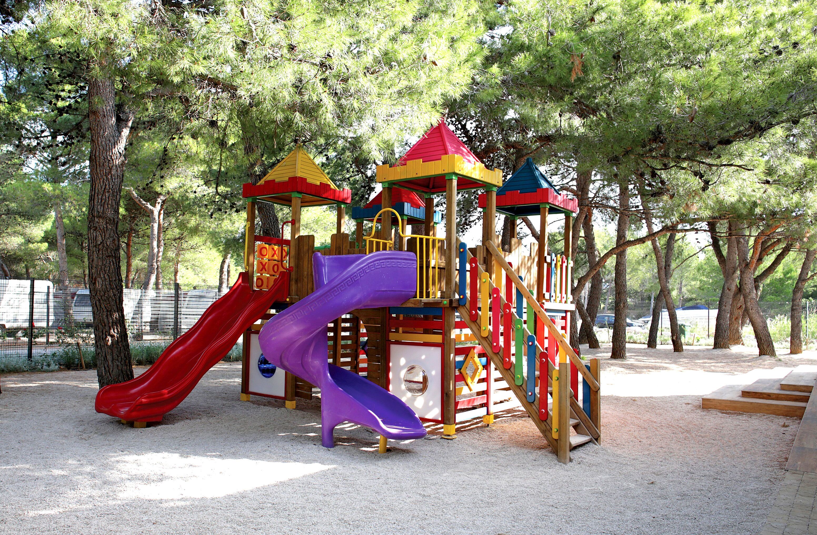 A playground with a red and purple slide, surrounded by trees.