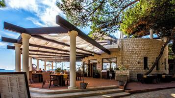 Ein Außenbereich zum Essen mit Steinsäulen, Tischen und Stühlen unter einer Pergola.