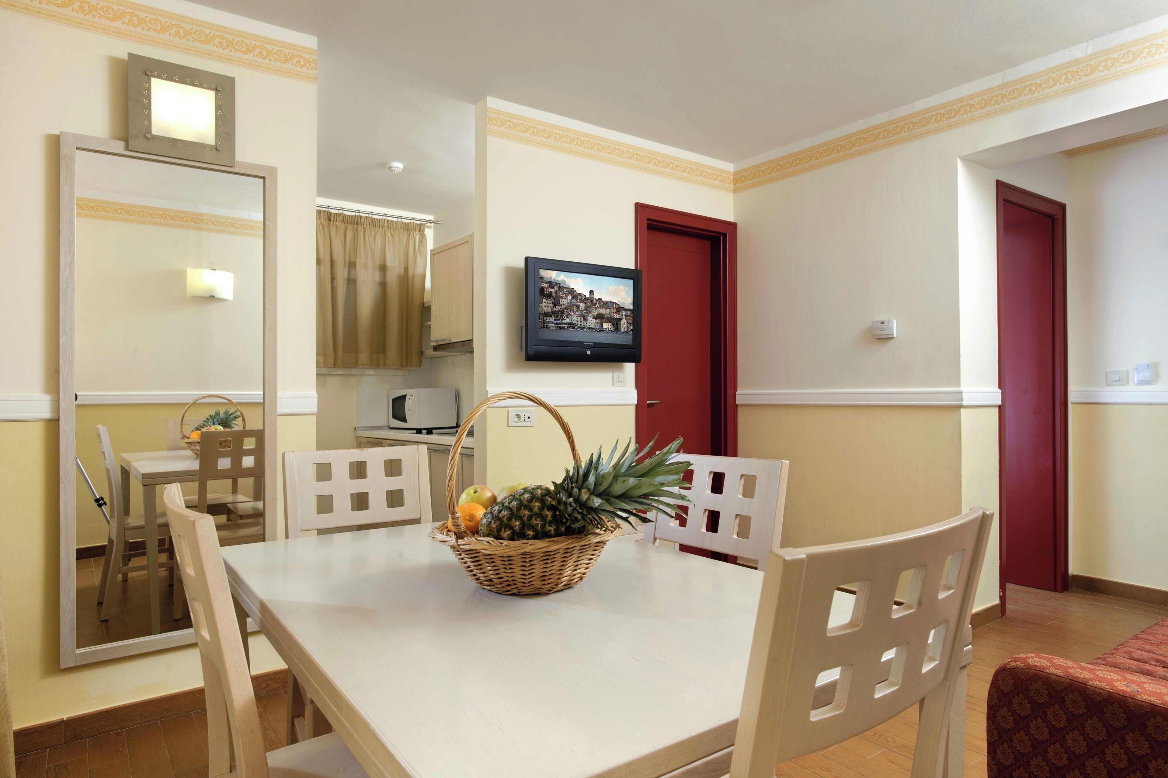 A dining area with a table, chairs, a television, and a red door.