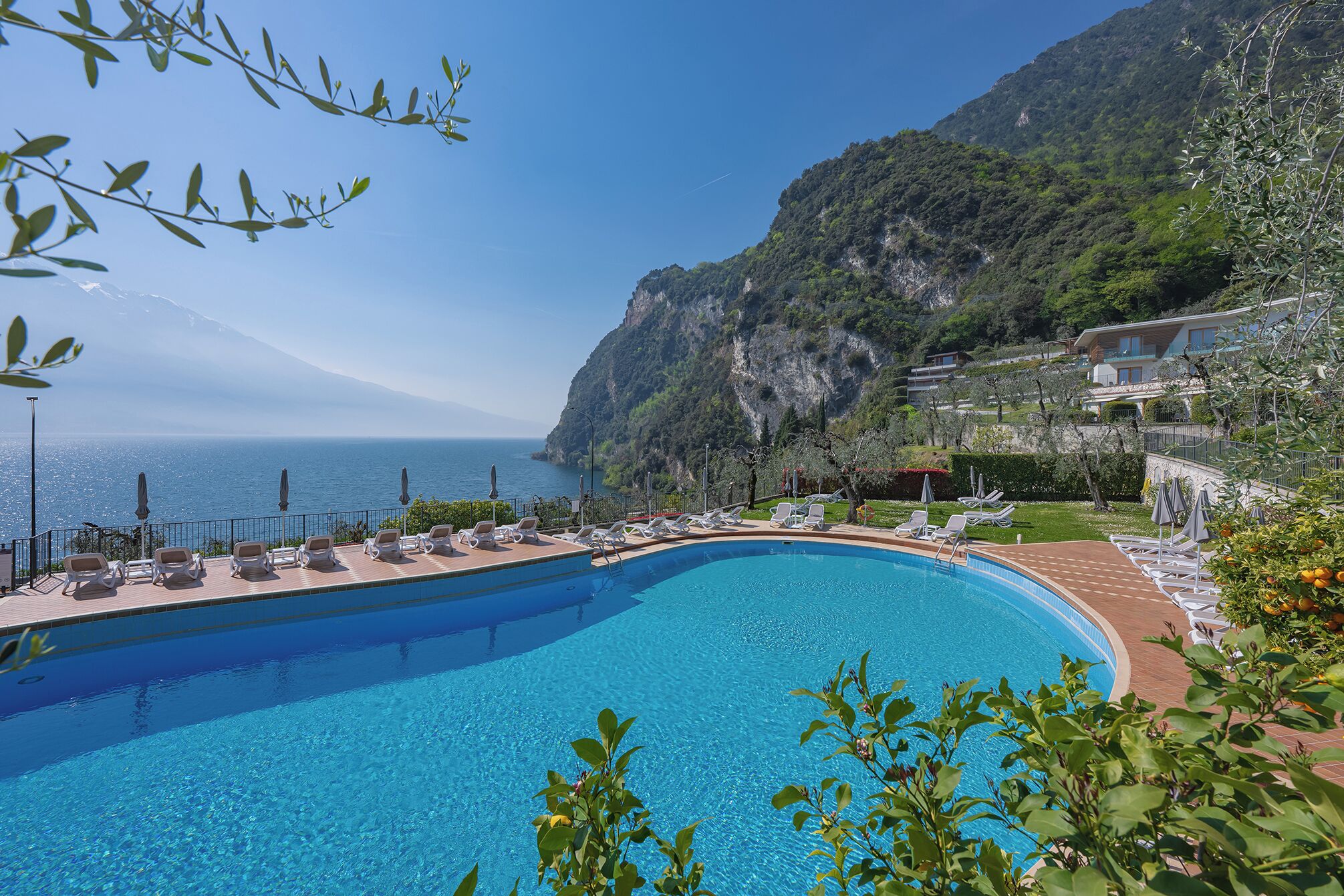 Une piscine bordée de chaises longues, une vue dégagée sur la mer et un paysage montagneux en toile de fond.