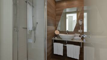 Ein modernes Badezimmer mit Duschkabine aus Glas, einem großen Spiegel, einem weißen Waschbecken und zwei Handtüchern.