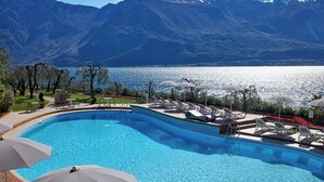 A swimming pool with lounge chairs and umbrellas, surrounded by mountains and a view of the lake. - Hotel Atilius Adults Only (Limone sul Garda)