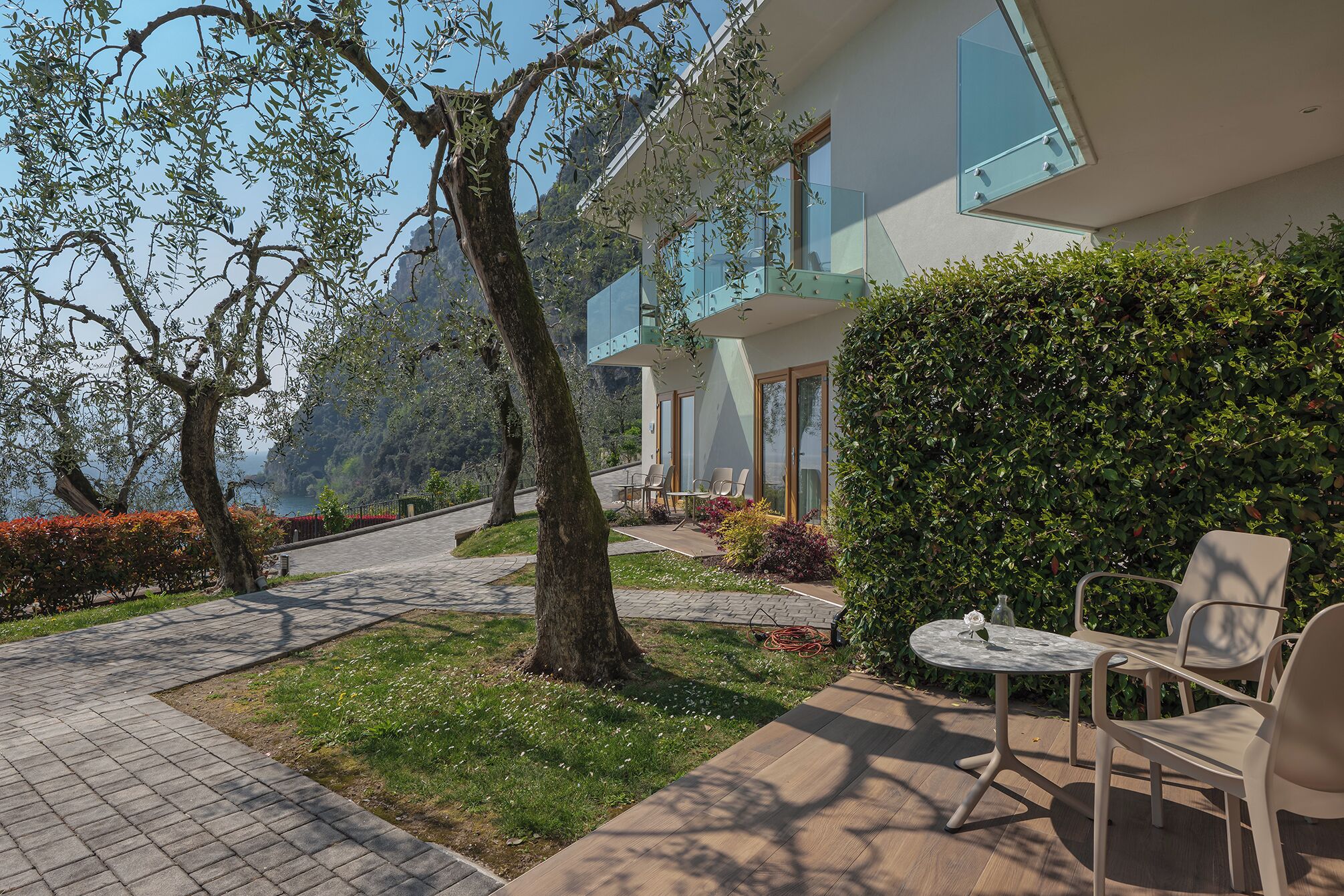 A modern building with a glass balcony, outdoor seating, and a pathway leading to the entrance.