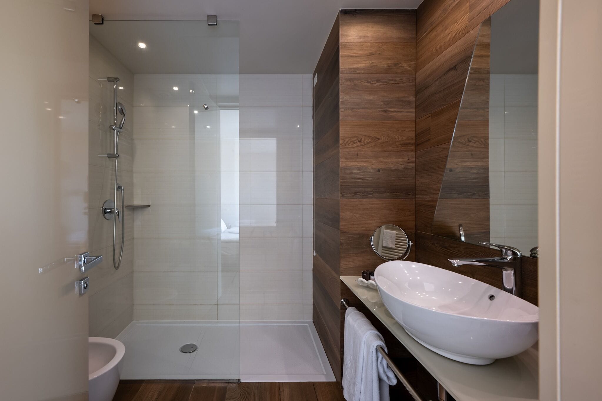 Une salle de bain moderne avec une douche à parois de verre, un lavabo blanc et un mur d’accent en bois.