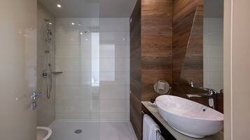 Une salle de bain moderne avec une douche à parois de verre, un lavabo blanc et un mur d’accent en bois.
