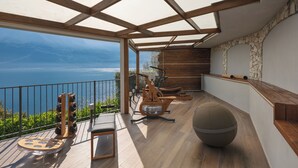 A balcony with a view of the sea, exercise equipment, and a round seating area. - Hotel Atilius Adults Only (Limone sul Garda)