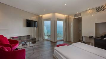 A modern hotel room with a bed, a TV, a dining area, and a balcony with a view.