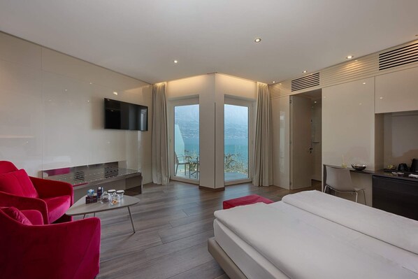 A modern hotel room with a bed, a TV, a dining area, and a balcony with a view.