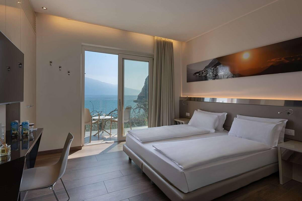 Ein Hotelzimmer mit Bett, Schreibtisch und Stuhl. Durch eine Schiebetür bietet sich Meerblick.