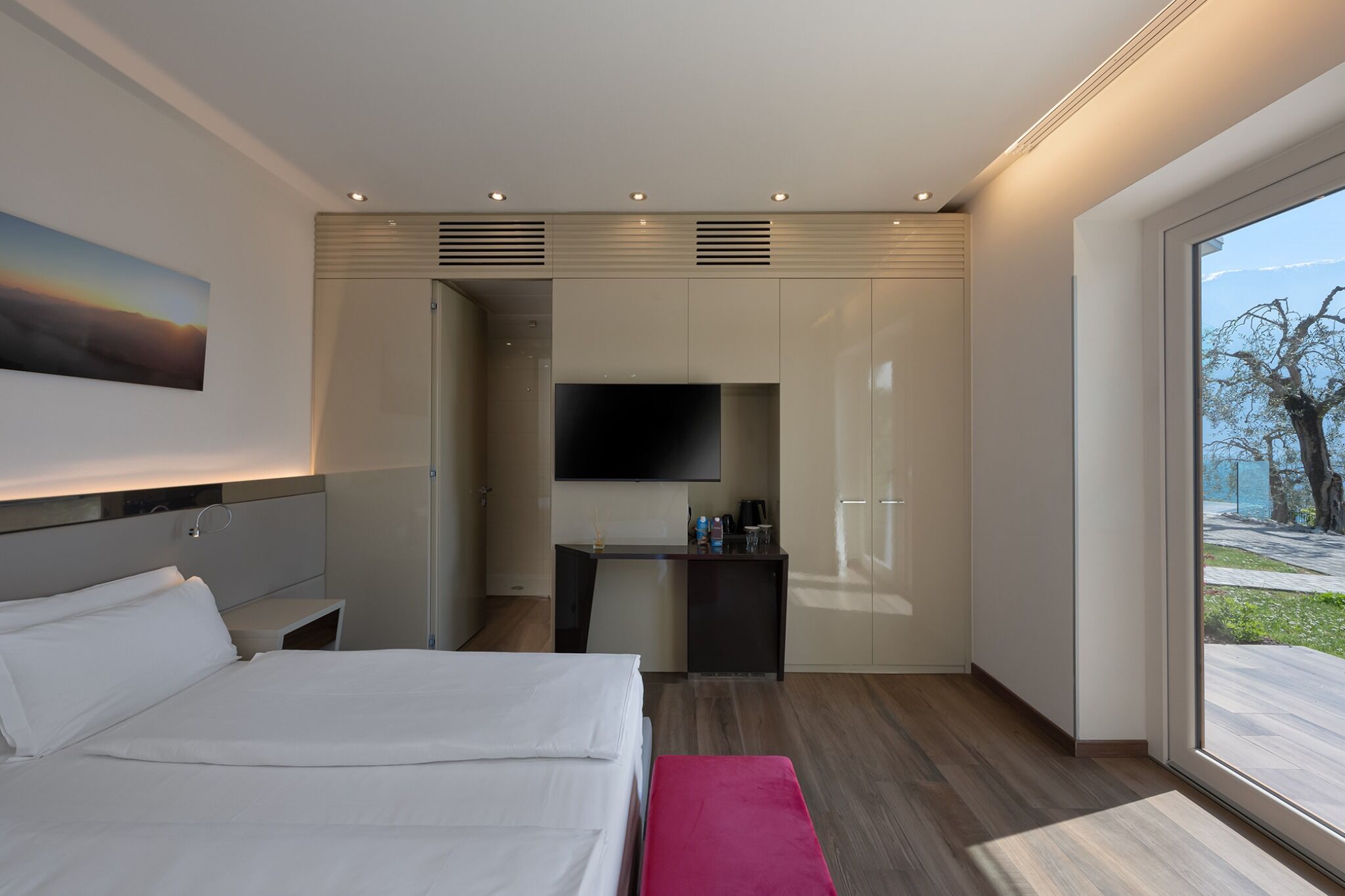 A modern hotel room with a bed, a desk, a TV, and a large window.