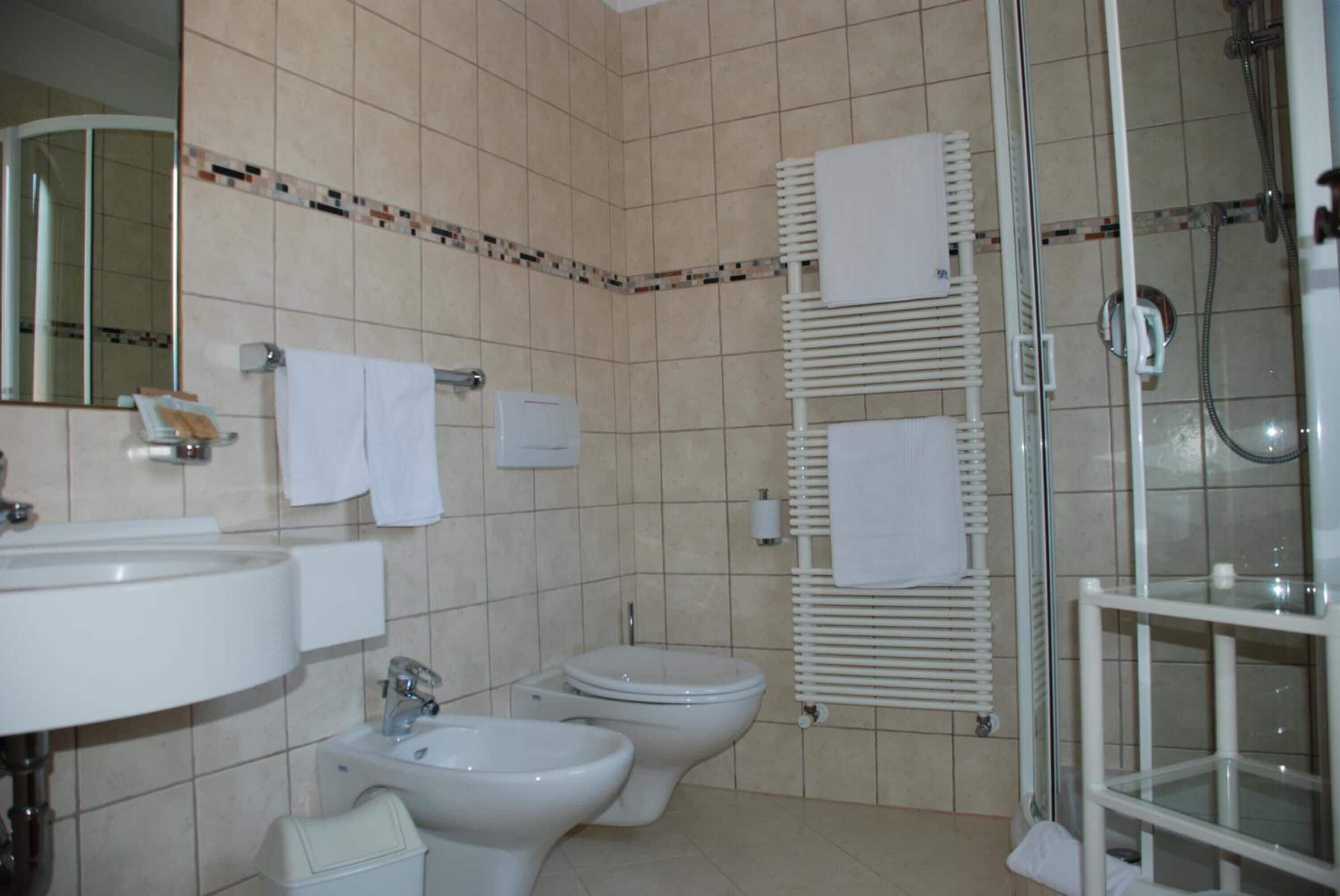 A bathroom with a sink, two toilets, a bidet, and a glass-enclosed shower.