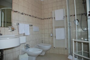 A bathroom with a sink, two toilets, a bidet, and a glass-enclosed shower. - Hotel Flora (Selva di Val Gardena)