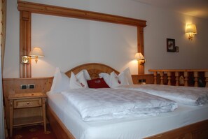 A double bed with a wooden headboard, two bedside tables with lamps, and a red accent pillow. - Hotel Flora (Selva di Val Gardena)