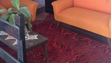 A room with a red patterned carpet, two orange sofas, a wooden chair, and a window with curtains.