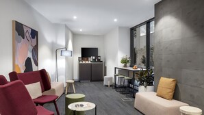 A modern living room with a sofa, chairs, a coffee table, and a kitchen area in the background. - Quest St Kilda Road (Melbourne)