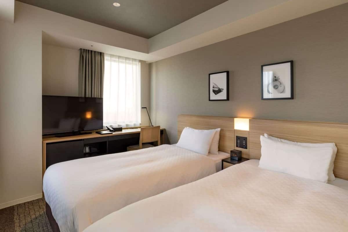 Una habitación de hotel con dos camas, un escritorio con televisor y cuadros en la pared.