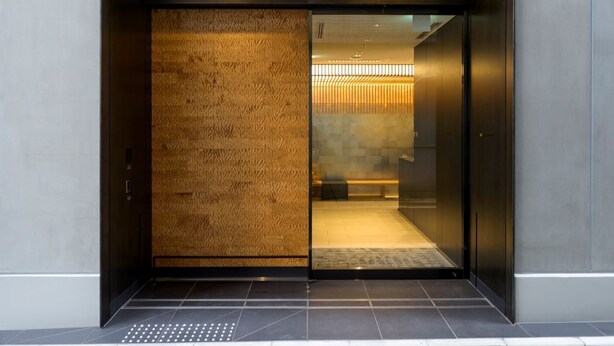 An elevator entrance with a wooden panel and glass doors, leading to a well-lit interior with a bench and a reception desk. - Best Western Hotel Fino Tokyo Akihabara (Tokyo)