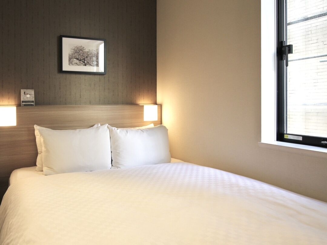 Habitación de hotel con cama, dos lámparas de noche, un cuadro en la pared y una ventana.