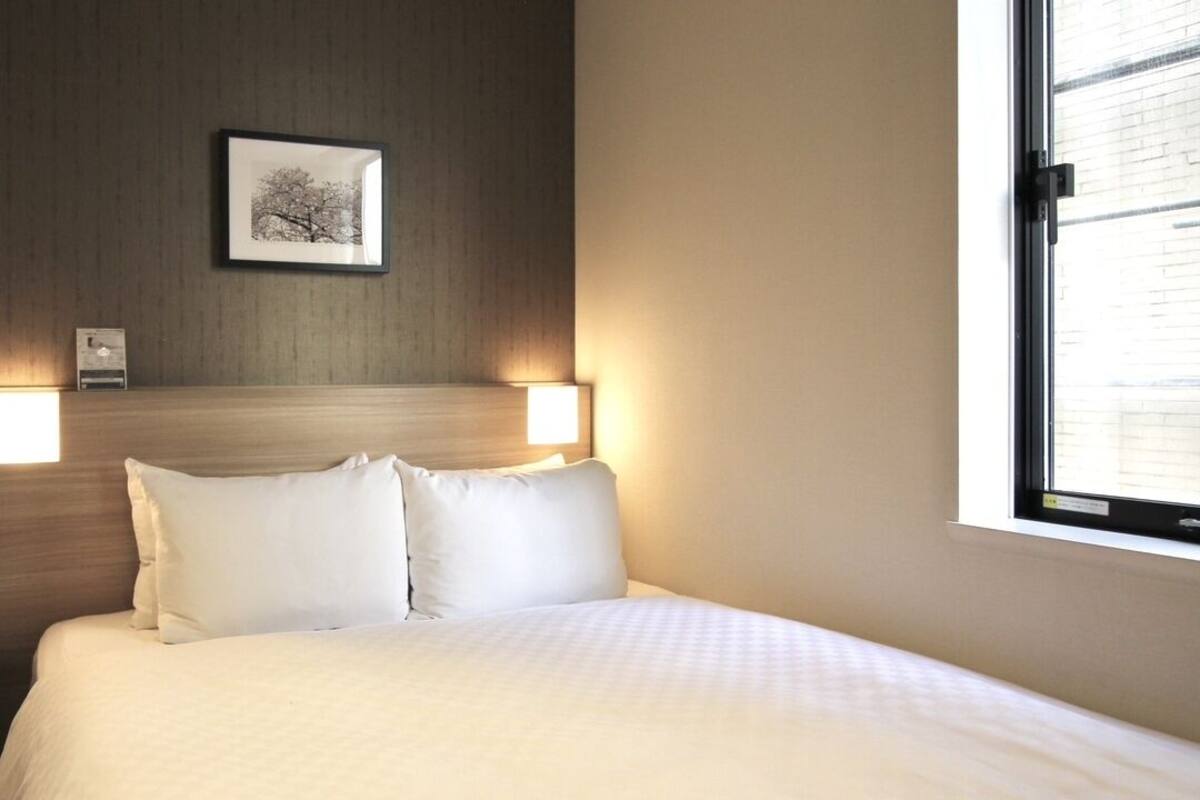 Habitación de hotel con cama, dos lámparas de noche, un cuadro en la pared y una ventana.