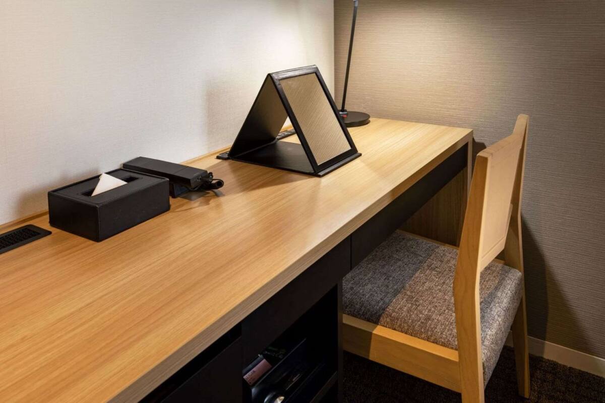 Un escritorio moderno con una laptop, una lámpara y una silla en una habitación de hotel.