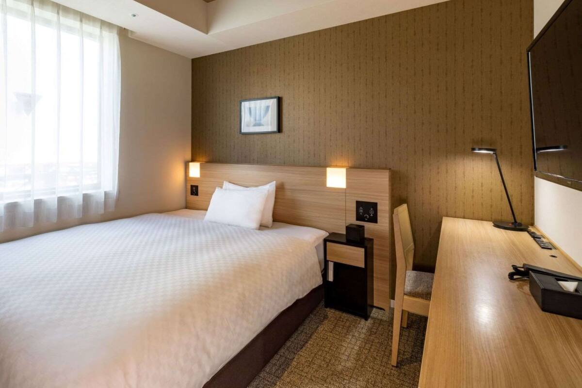 Habitación de hotel con una cama grande, un escritorio, una silla y un televisor.