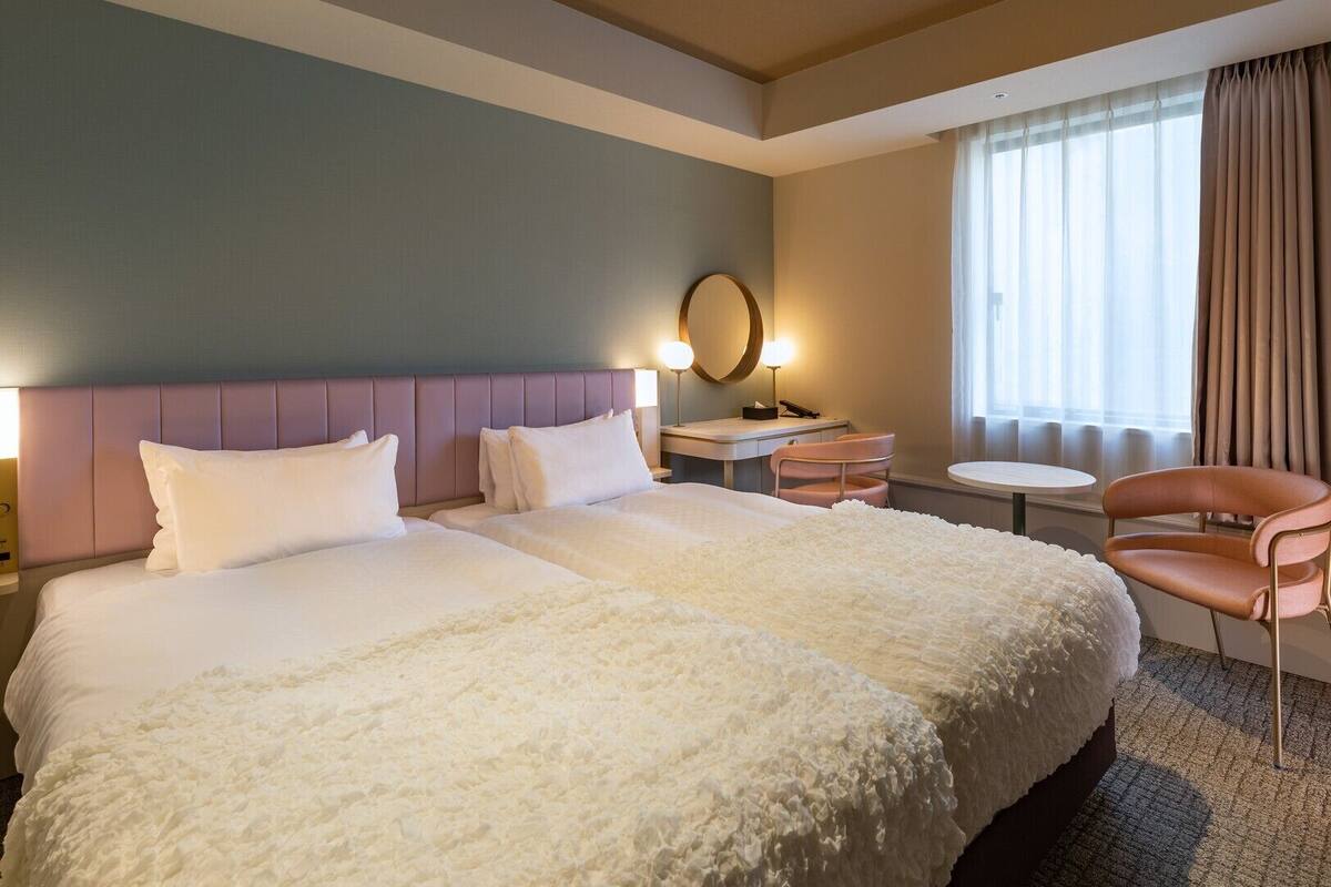 Habitación de hotel con una cama grande, una mesita de noche, una silla, un escritorio y una ventana con cortinas.