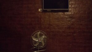 Una habitación con pared de madera, televisor montado y ventilador de pie.