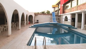 Una piscina interior con un tobogán azul, arcos blancos y un edificio con un letrero que dice "KAMIKASE MONTENEGRO".