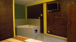 Habitación de hotel con una cama grande, una bañera integrada y un televisor montado en la pared.