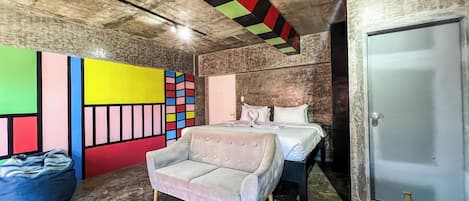 A bedroom with a bed, a chair, a colorful wall art, and a door.